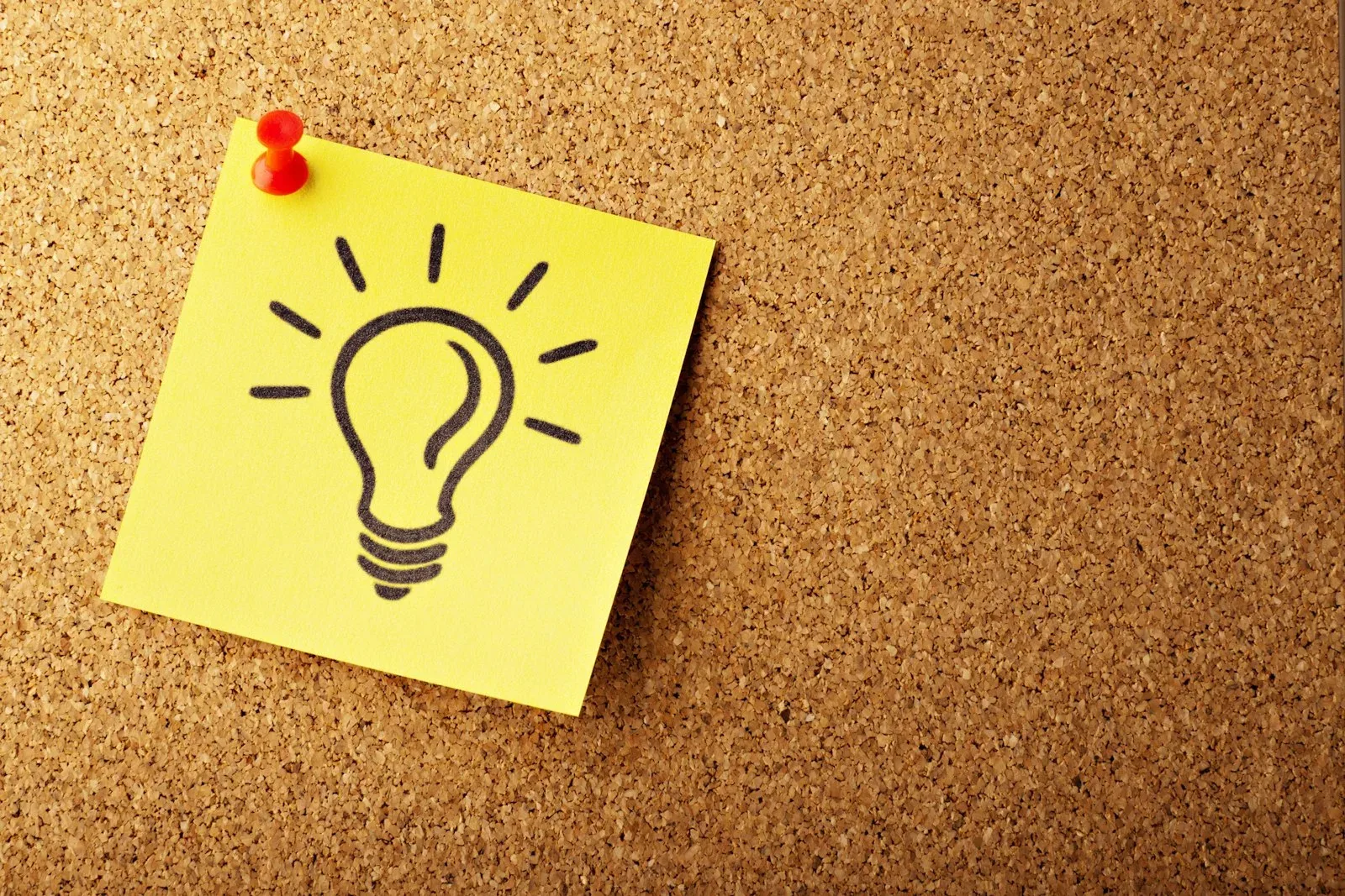 Post-it amarelo com desenho de lâmpada em um quadro de cortiça